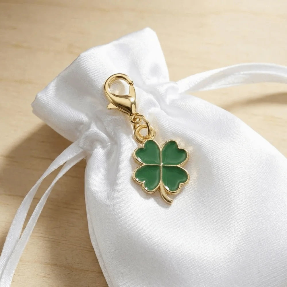 Gold-toned four leaf clover keychain attached to a white fabric drawstring bag