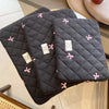 A dark gray quilted slim laptop sleeve with pink embroidered hearts resting on a light surface.