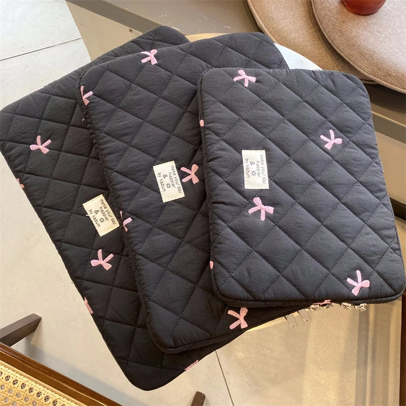 A dark gray quilted slim laptop sleeve with pink embroidered hearts resting on a light surface.