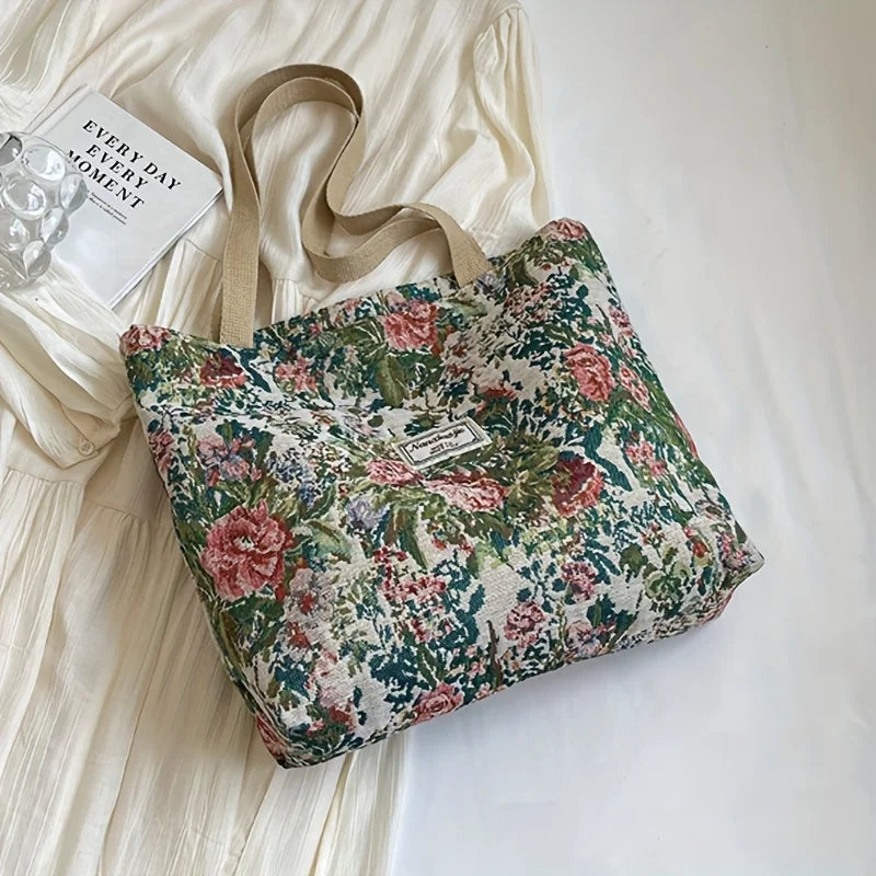 A floral patterned bohemian corduroy tote bag resting on a white surface next to a piece of light-colored fabric.
