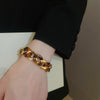 A close-up of a hand wearing a gold-toned interlocking chain bracelet with amber leopard print accents.