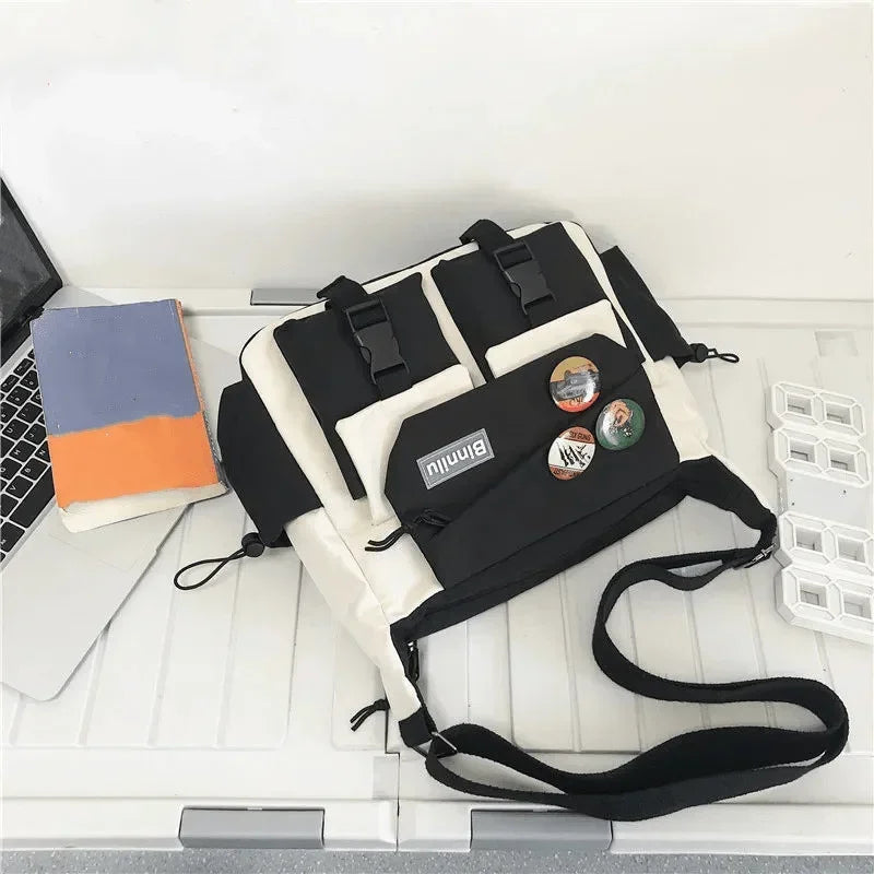 Bolso cruz de nylon casual blanco y negro con múltiples compartimentos y correas sobre una superficie blanca.