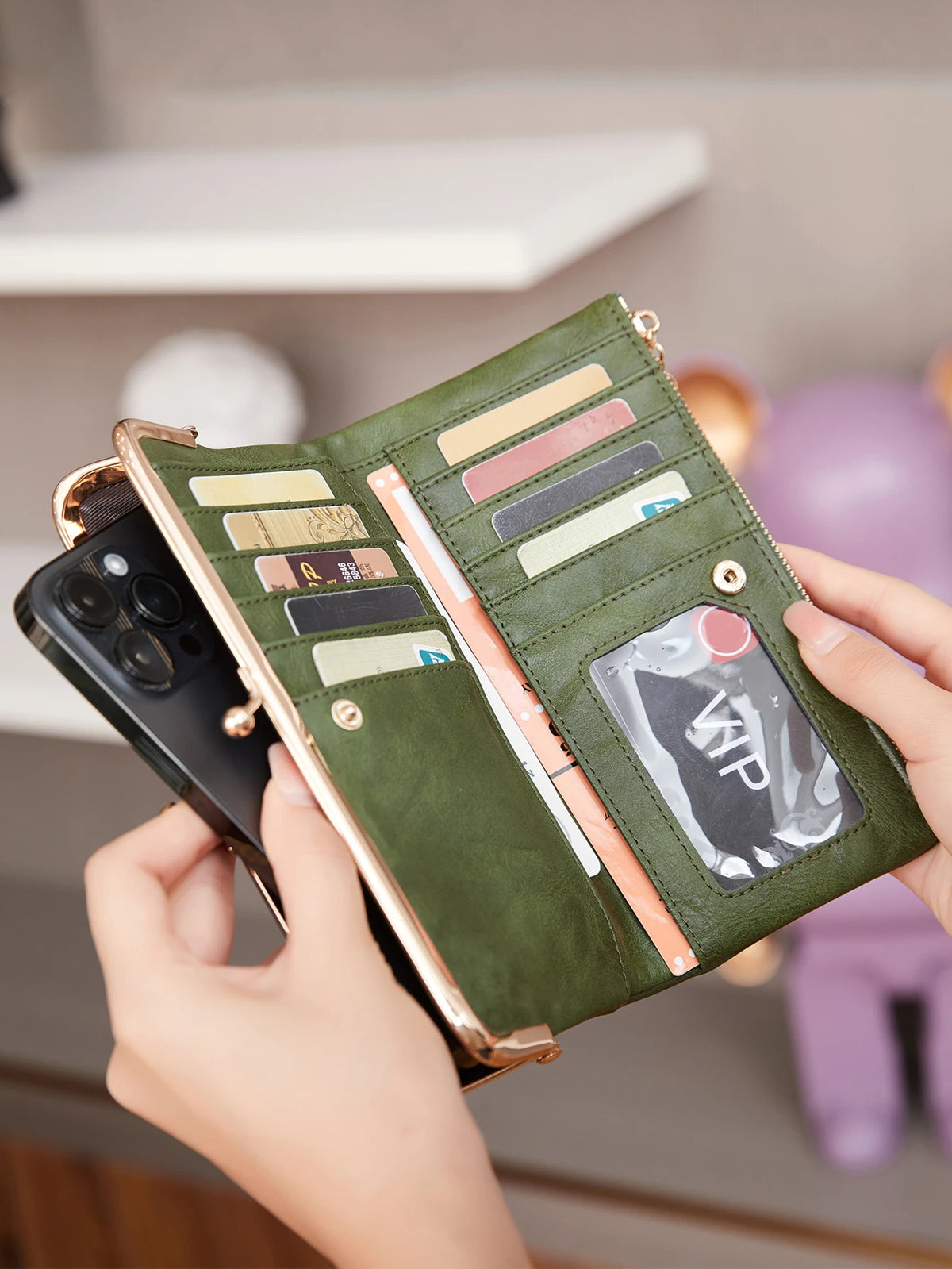 Eine Hand hält eine offene olivgrüne Vintage-Reißverschlus-Geldbörse mit verschiedenen Karten und einem Telefon.