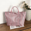 A striped transparent PVC tote bag with pink and green vertical stripes resting on a wooden surface.