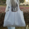 A person holds a striped grocery tote bag with a brown handle against a blurred outdoor background.