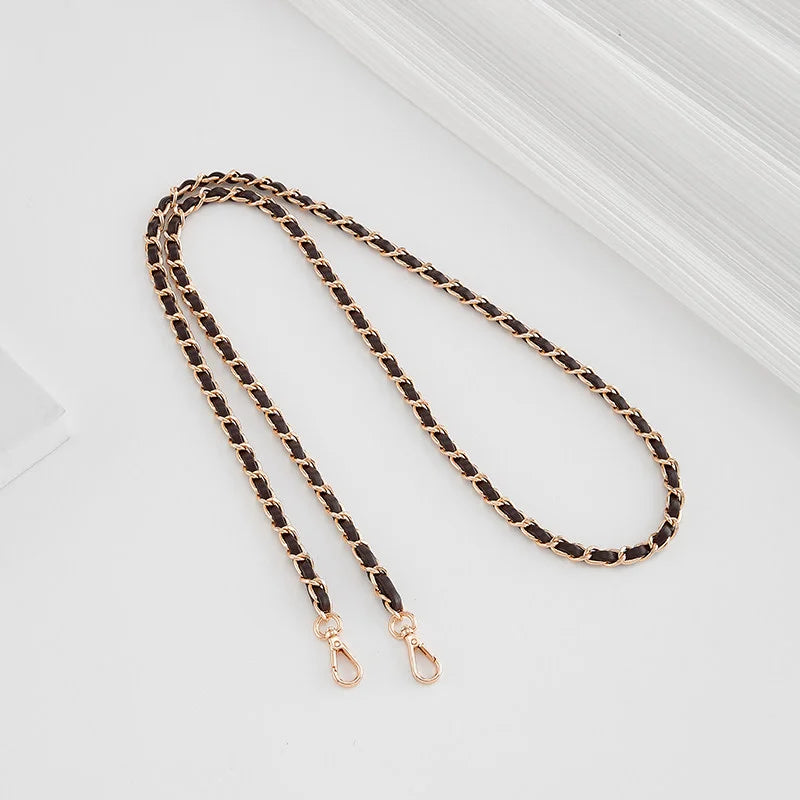 A close-up of a black and gold braided leather strap with a buckle, laid diagonally on a light surface.
