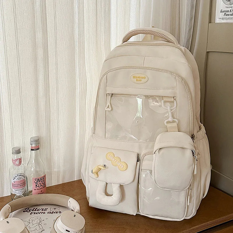 A cream-colored Kawaii Harajuku backpack with a clear laptop compartment and multiple pockets is displayed on a wooden surfac