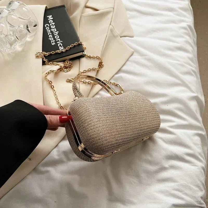 A beige glitter crossbody evening clutch bag resting on a white sheet next to a book.