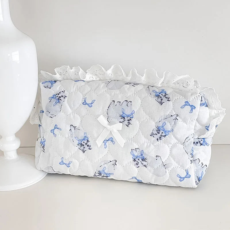 White quilted cosmetic storage pouch with blue floral embroidery and ruffled edge