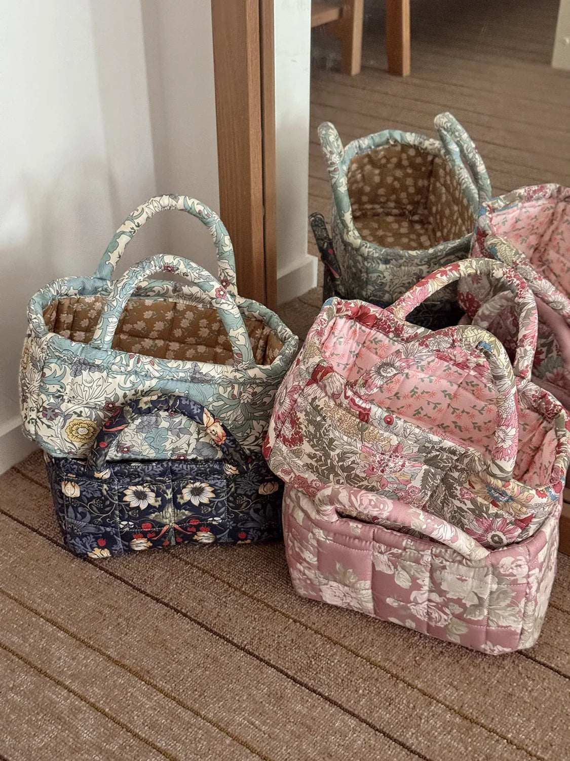 A collection of quilted fabric storage baskets in various floral patterns and colors resting on a wooden floor.