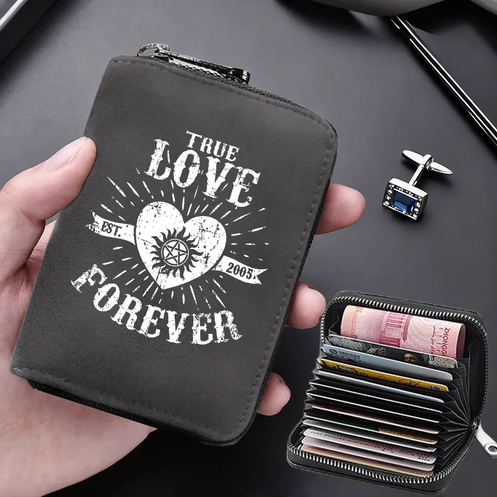 A dark gray compact card wallet with the text True Love Forever embossed on it, shown being held next to a stack of credit ca