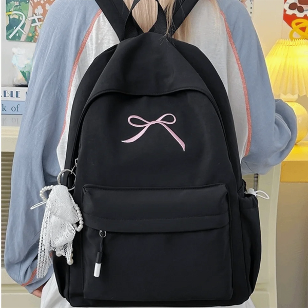 A black nylon backpack with a pink bow embroidery and a white tassel attached to the strap.