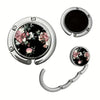 Silver bag hook with a circular design featuring pink and green floral patterns.