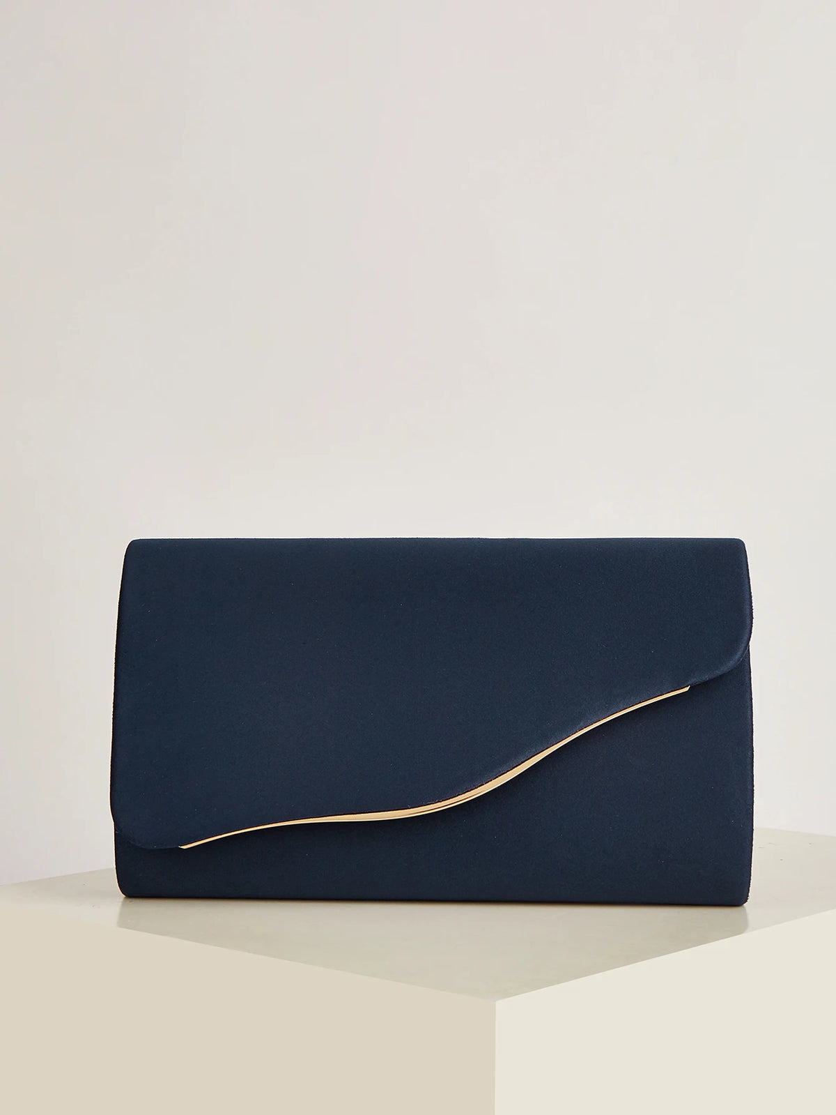 A dark navy velvet evening clutch with a gold-toned fold detail resting on a light surface.