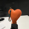 Cartera de monedas con forma de corazón naranja de PU y correa de cuero negro, sostenida contra un fondo oscuro.