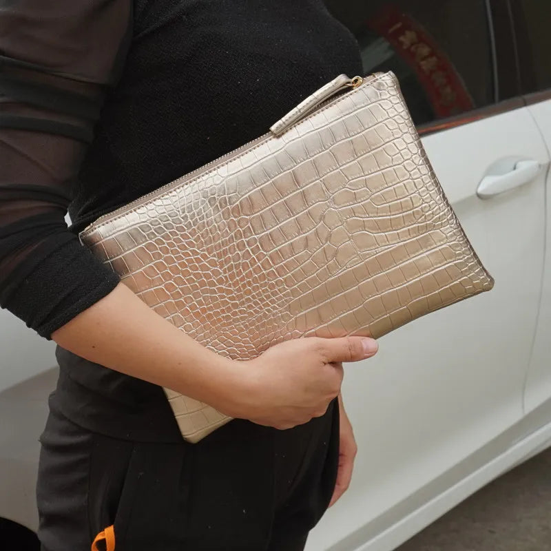 A person holds a gold-toned alligator print clutch bag against a white car door.