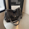 A dark gray denim tote bag with a textured finish and a silver chain strap is displayed on a light surface.