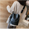 A woman wearing a cream sweater holds a black alligator pattern leather crossbody bag.