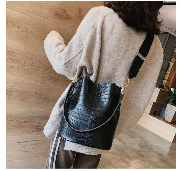 A woman wearing a cream sweater holds a black alligator pattern leather crossbody bag.