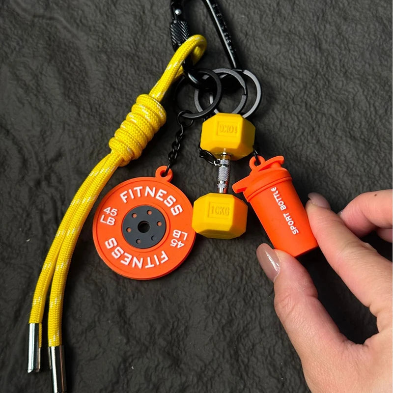 A yellow nylon D-shape fitness keychain with an orange tag and a small yellow bottle attached to a black keyring.