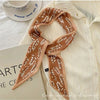 Un foulard floral en soie marron drapé autour d'une chemise blanche à col, avec une tasse blanche visible en arrière-plan.