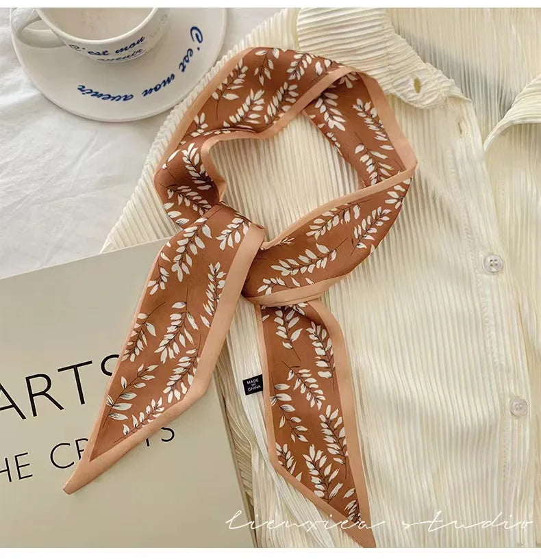 Un foulard floral en soie marron drapé autour d'une chemise blanche à col, avec une tasse blanche visible en arrière-plan.