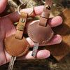A hand holds a genuine leather key fob cover with a keychain ring and a small metal key.