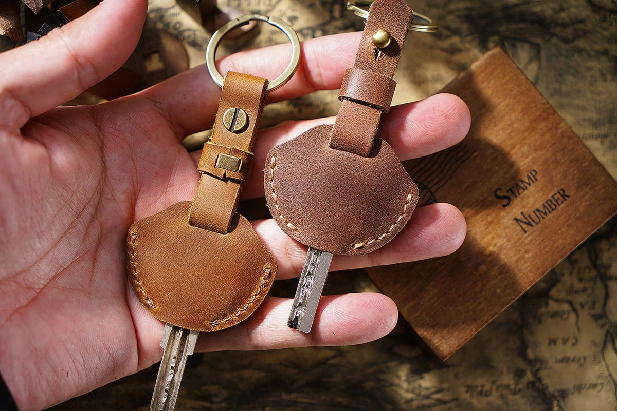 A hand holds a genuine leather key fob cover with a keychain ring and a small metal key.