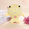 A yellow shark mini plush toy with pink accents and white polka dots lying on a light surface.