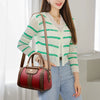 A woman is holding a red leather shoulder crossbody bag with brown trim and a light green striped cardigan.