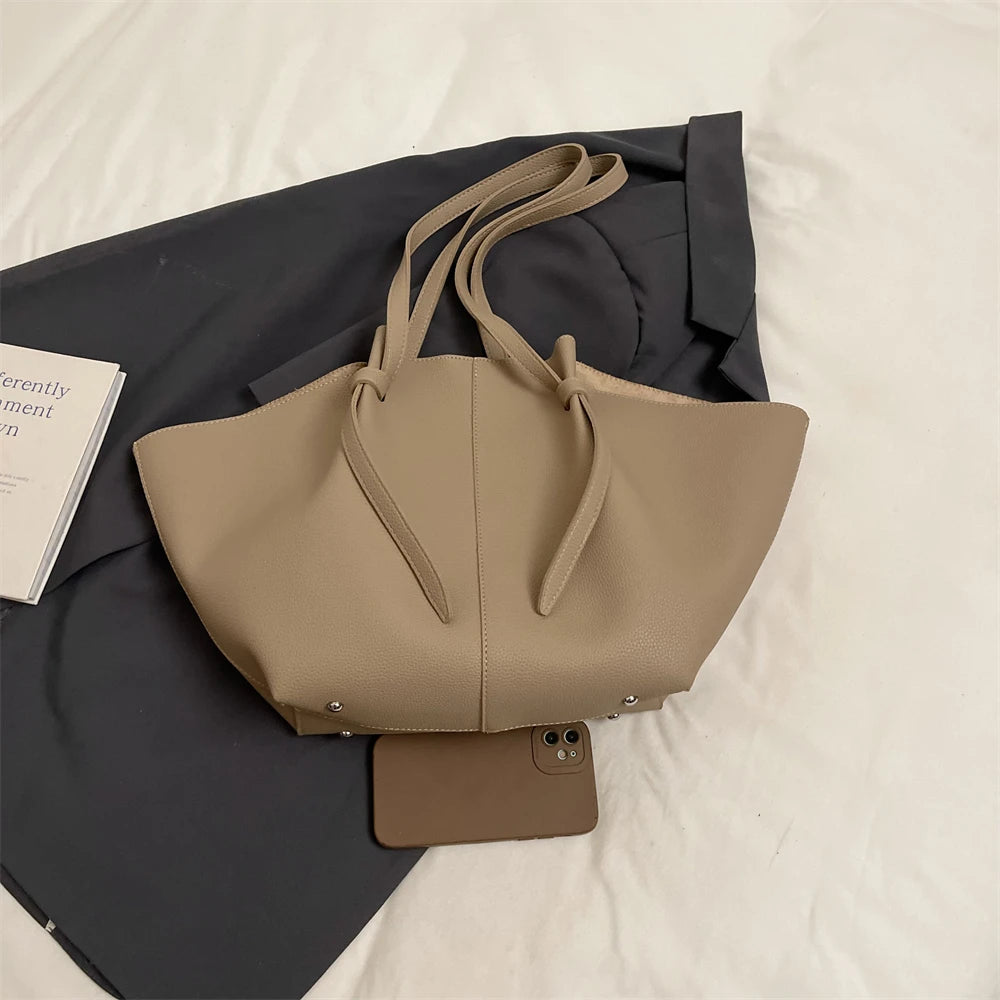 A beige luxury PU leather shoulder tote bag is displayed on a dark fabric against a white background.