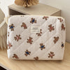 A cream-colored quilted cosmetic makeup bag featuring small brown teddy bear embroidery.