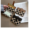 A hand holds a checkered black and tan PU leather mini card wallet next to some paper.