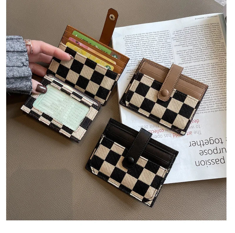 A hand holds a checkered black and tan PU leather mini card wallet next to some paper.