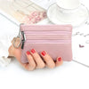 A pink PU leather clutch wallet with silver hardware is held in a person's hand next to a white cup and some paper.