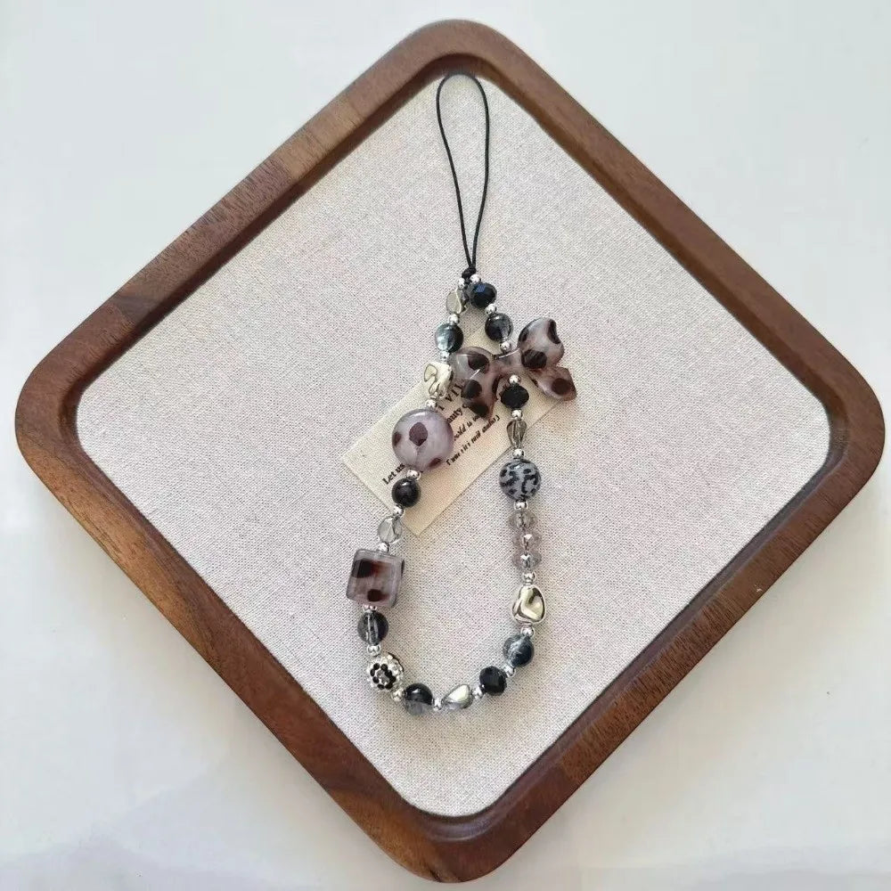 Leopard print bowknot phone lanyard featuring heart and various beads displayed on a wooden tray.