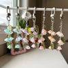 A display of handmade Lily of the Valley flower keychains featuring pastel pink and blue blossoms on green stems.