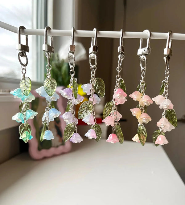 A display of handmade Lily of the Valley flower keychains featuring pastel pink and blue blossoms on green stems.