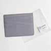Porte-cartes en cuir véritable gris avec texture, montré dans une gaine en plastique transparent.