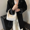 A woman holds a woven embossed hobo shoulder bag with a top handle in front of a black coat and light-colored pants.