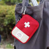 A red and white first aid kit pouch hanging from a gray fabric tote bag.