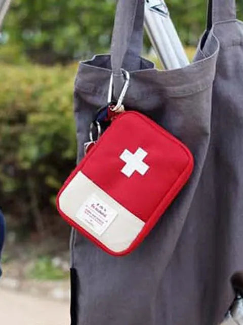 A red and white first aid kit pouch hanging from a gray fabric tote bag.