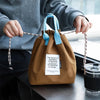 A brown waterproof insulated lunch bag with blue drawstring is held by a person.
