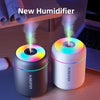 A white humidifier emits a plume of mist on a wooden desk next to a laptop.