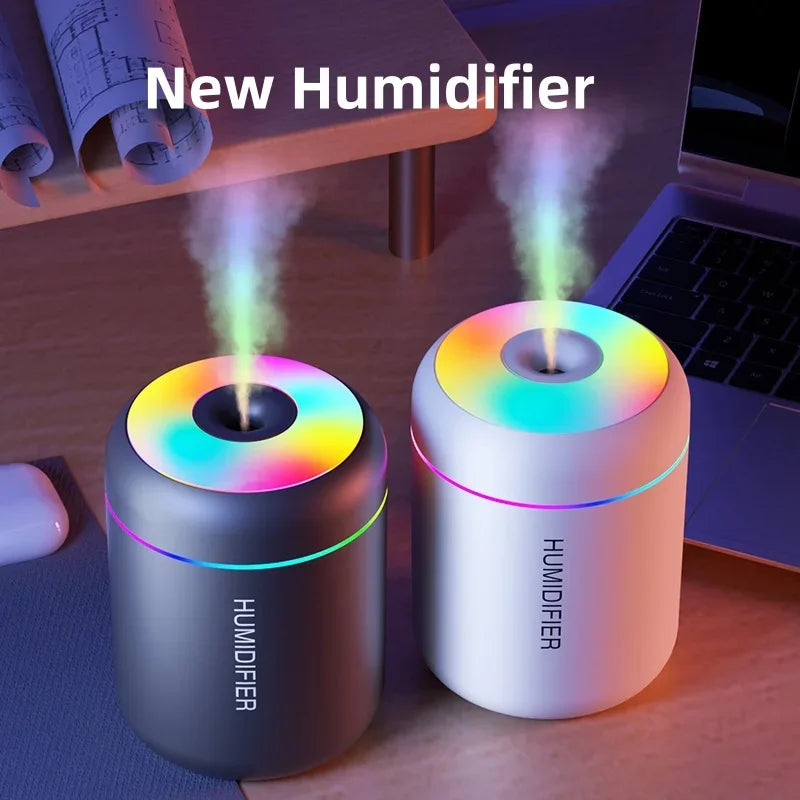 A white humidifier emits a plume of mist on a wooden desk next to a laptop.