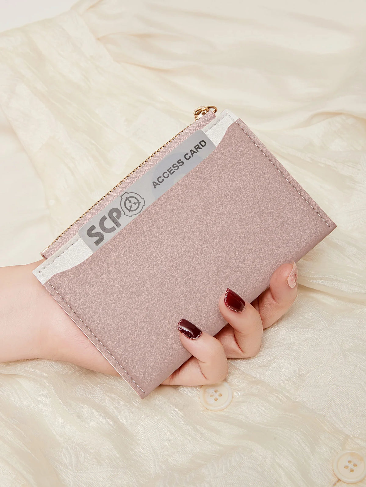 Une main tient un porte-cartes en cuir PU rose pâle minimaliste avec une boucle dorée sur fond crème.