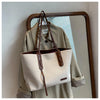 A beige canvas shoulder tote bag is displayed next to a light green shirt in front of a mirror.
