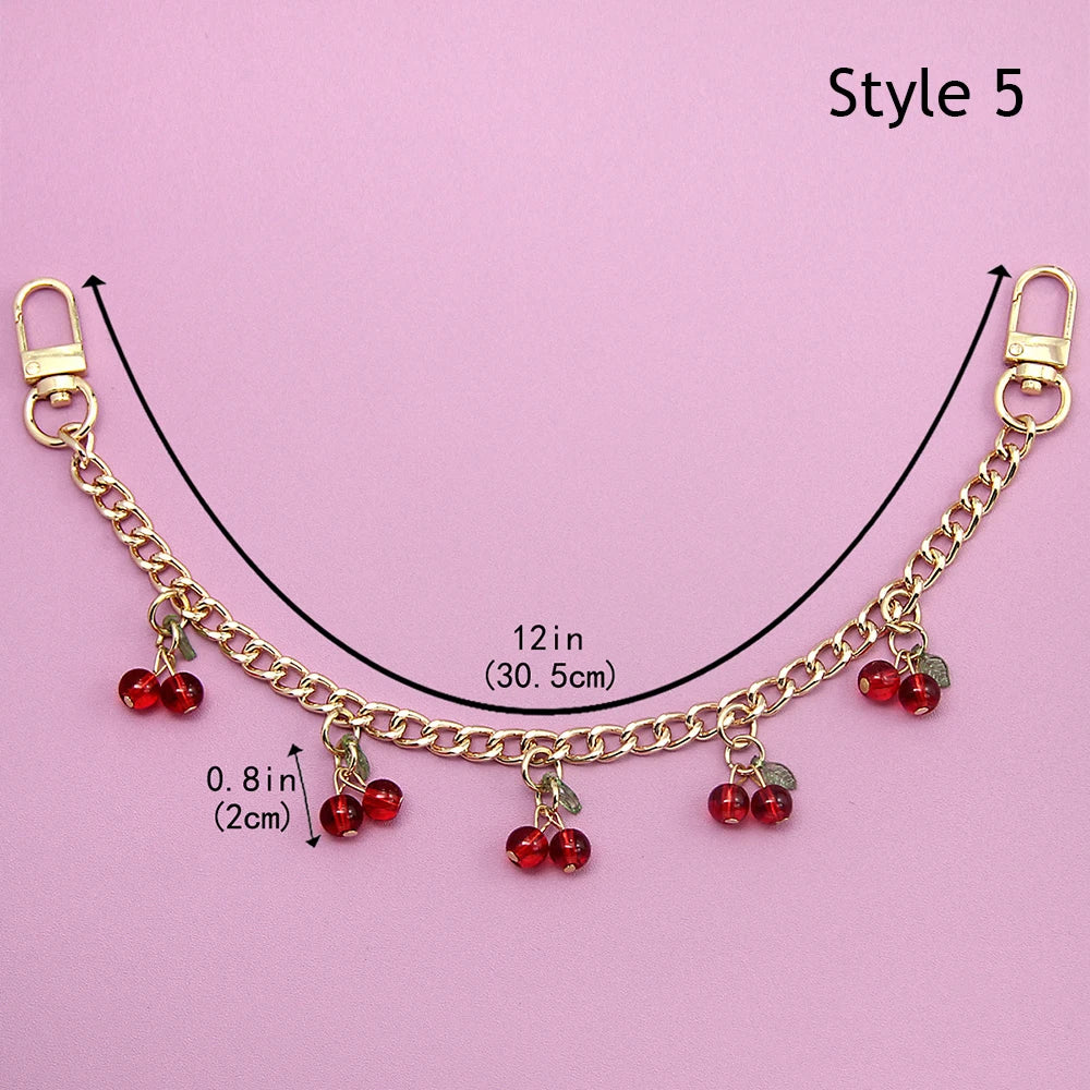Accesorio de cadena dorada con corazones de esmalte y flores de cerezo, mostrado contra un fondo rosa.