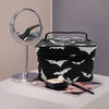 Bolsa portátil de maquillaje con temática de murciélago en blanco y negro junto a un espejo de aumento plateado.