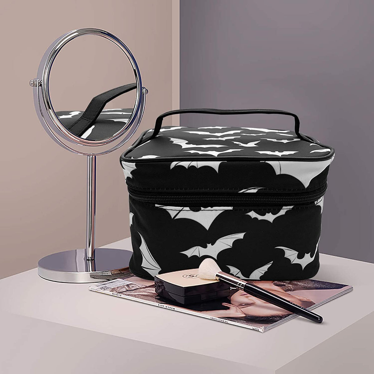Bolsa portátil de maquillaje con temática de murciélago en blanco y negro junto a un espejo de aumento plateado.